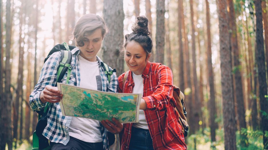 A young couple with backpacks exploring a forest using a map. Adventure and travel concept.