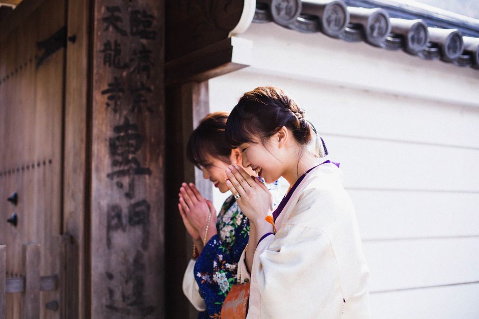 Two women in kimonos praying at a Kyoto temple gate, embracing Japanese tradition.